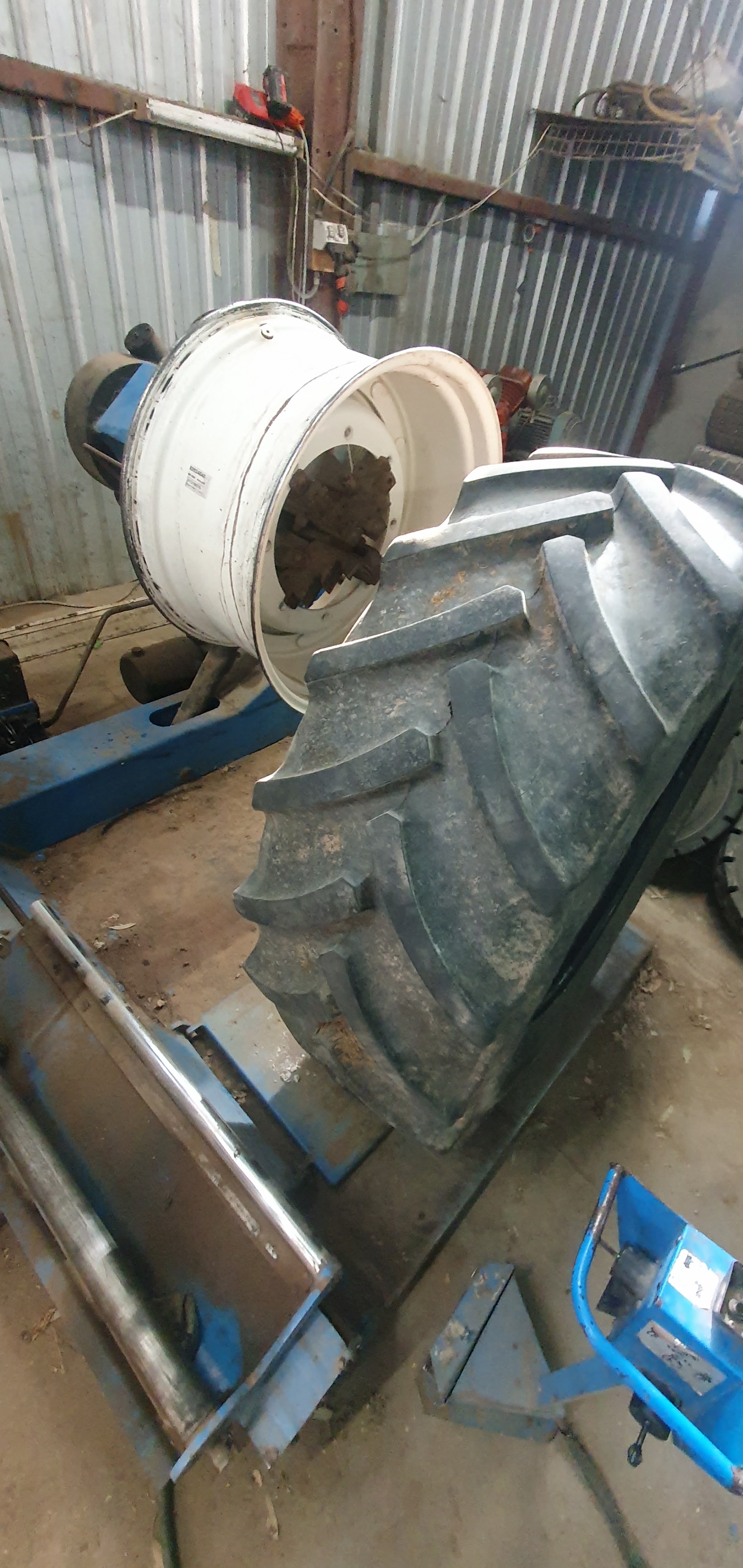 A large tractor tyre being fitted to a white agricultural rim on the tyre changer