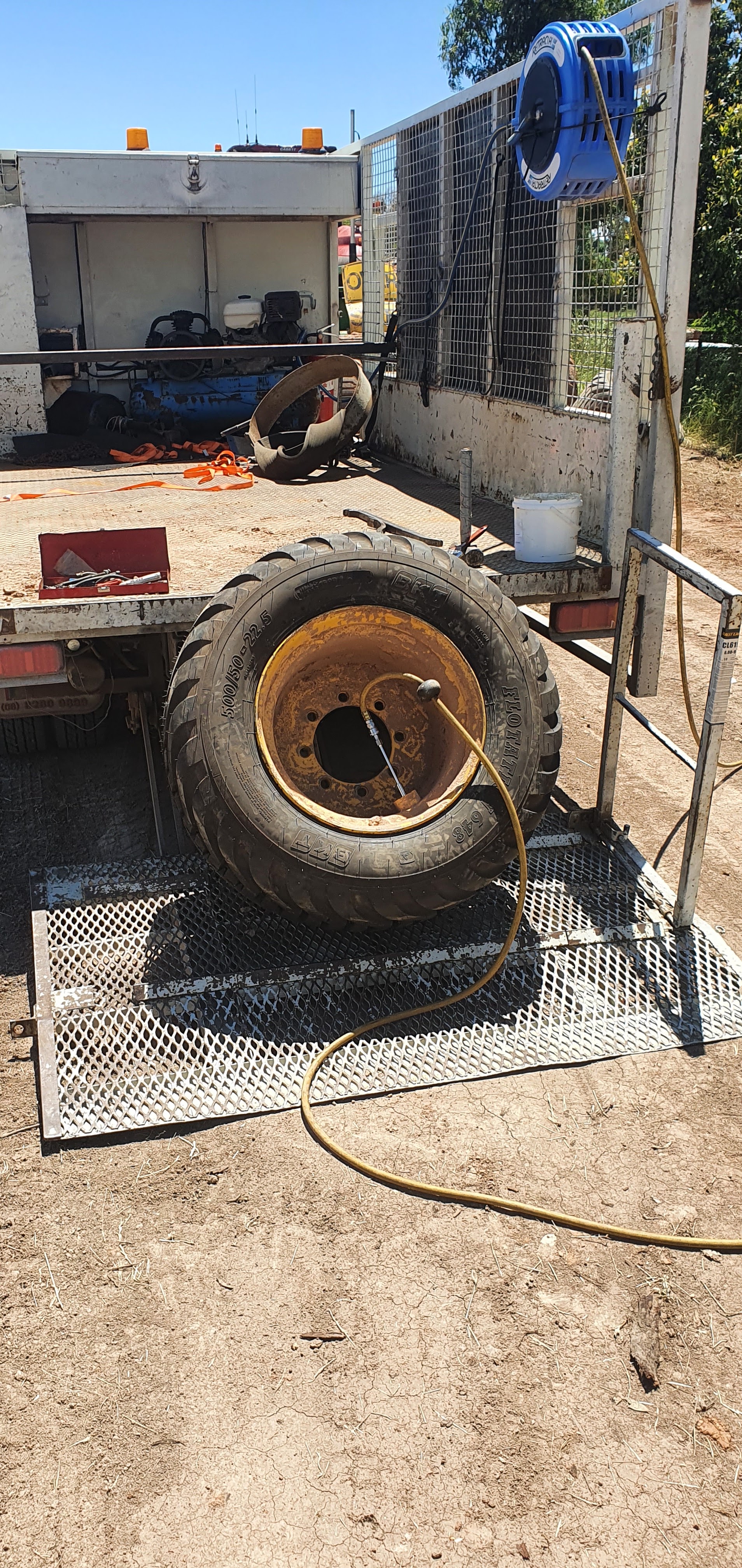 A truck mounted tyre rig with the air line run out, changing a large flotation tyre on a ramp in a paddock